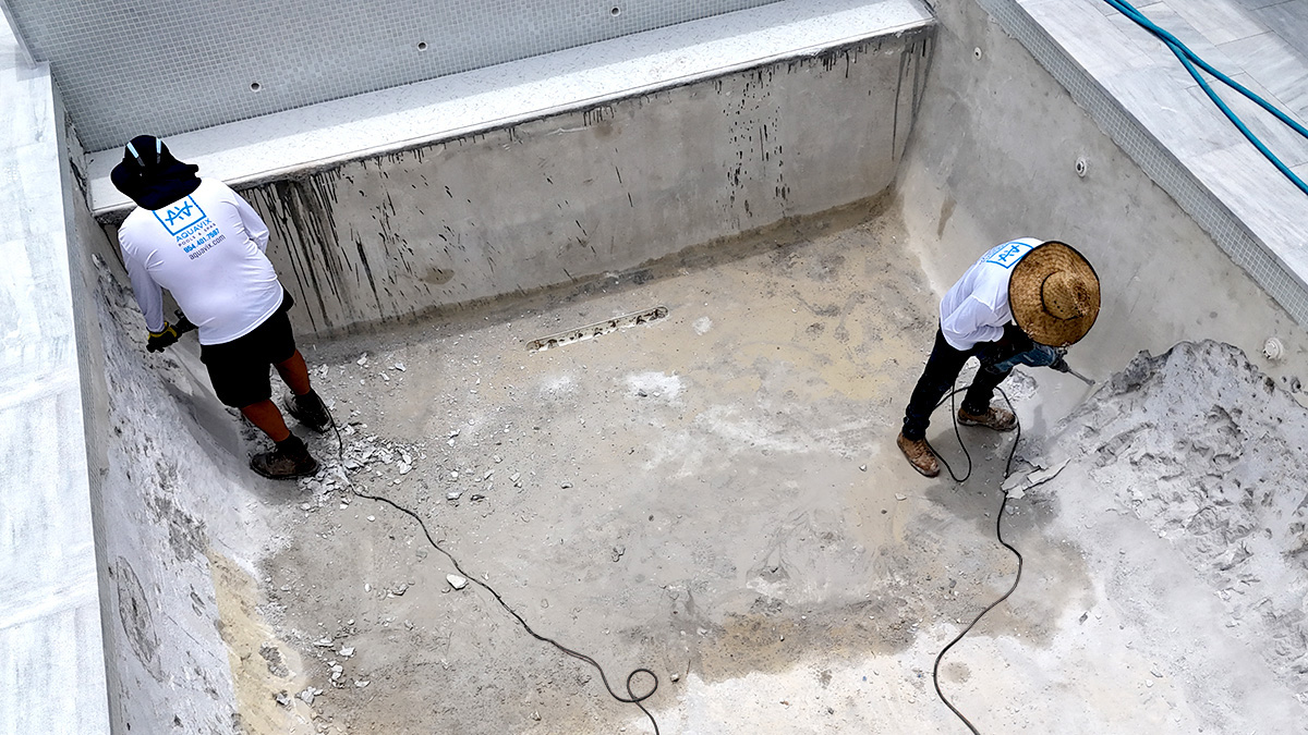 Workers removing old plaster from a swimming pool during resurfacing.